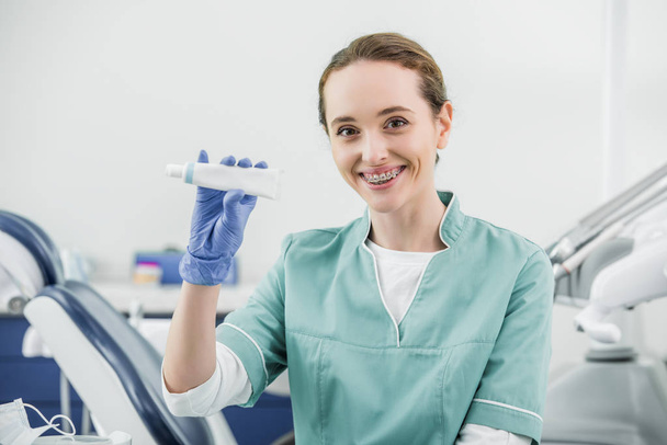 wesoły kobieta dentysty z szelkami na gospodarstwa Pasta do zębów  - Zdjęcie, obraz
