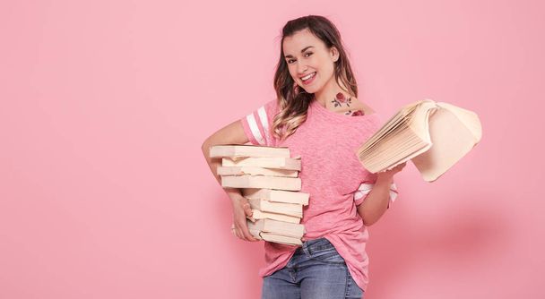 Horizontal portrait of a girl with a stack of books, on a pink background, lifestyle and education concept - Photo, Image