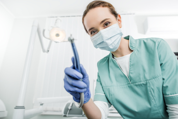 selective focus of dentist in mask and latex gloves holding dental drill - Φωτογραφία, εικόνα