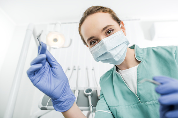 enfoque selectivo del dentista femenino en guantes de látex y máscara que sostiene instrumentos dentales
 - Foto, Imagen