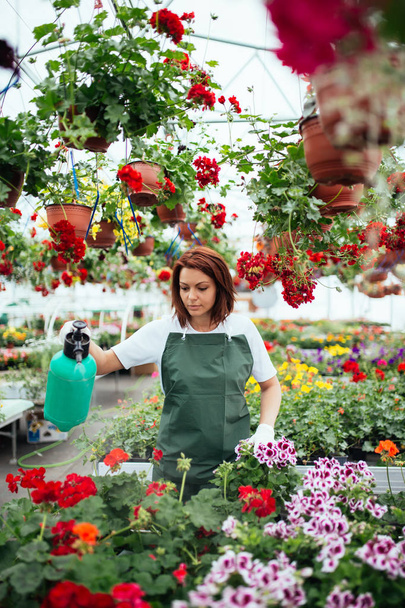 Redhead young woman working in greenhouse and enjoying in beautiful flowers. Female worker working at garden center. - Zdjęcie, obraz