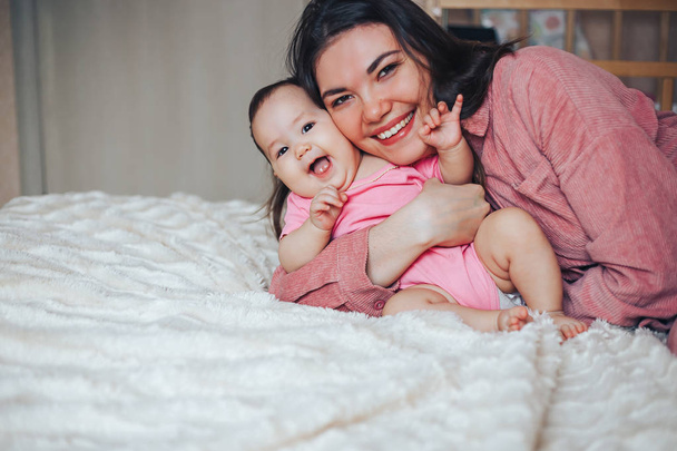 Madre y bebé con ropa rosa jugando y riendo. Un feliz día de las madres de familia
 - Foto, imagen