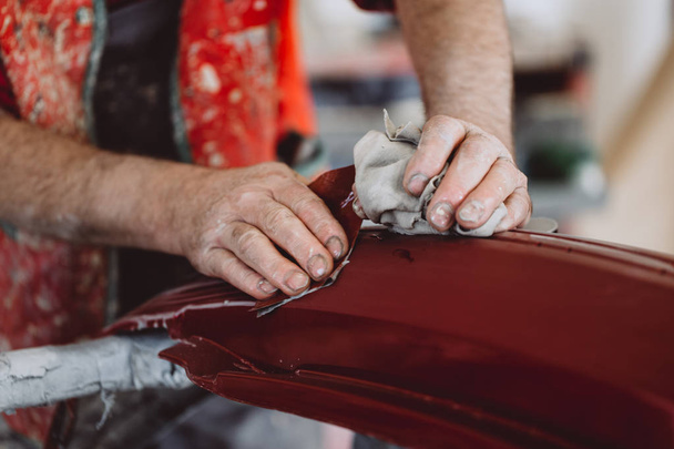 Car detailing - Man with sandpaper in auto repair shop sanding polishing and preparing car parts for painting. Selective focus on man's hand. - Фото, изображение