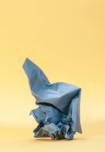 Crumpled blue paper on a pastel yellow background. - Photo, Image
