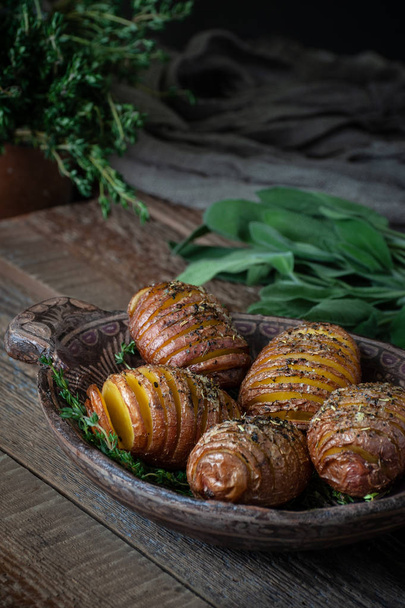 Whole baked potatoes with thyme in a wooden plate on an old rustic table. - 写真・画像