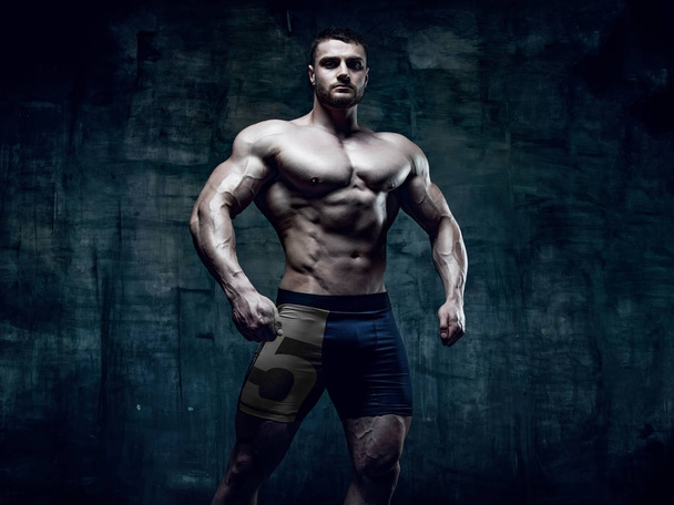 Gespierde bodybuilder man poseren in studio op grunge achtergrond - Foto, afbeelding
