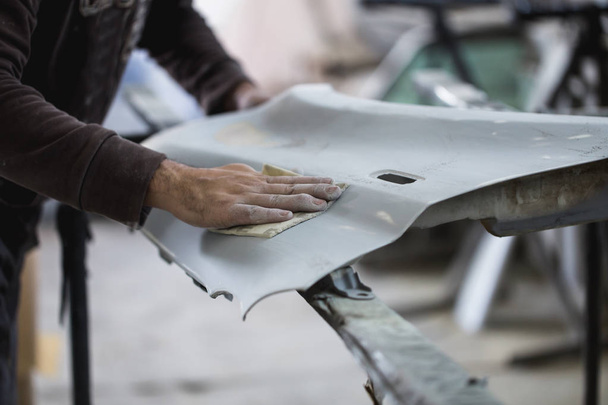 Car detailing - Man with sandpaper in auto repair shop sanding polishing and preparing car parts for painting. Selective focus on man's hand. - Φωτογραφία, εικόνα