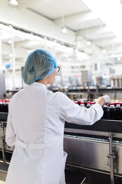 Serious middle age woman quality control worker checking robotic line for bottling and packaging carbonated black juice of soft drink into bottles. - Photo, Image