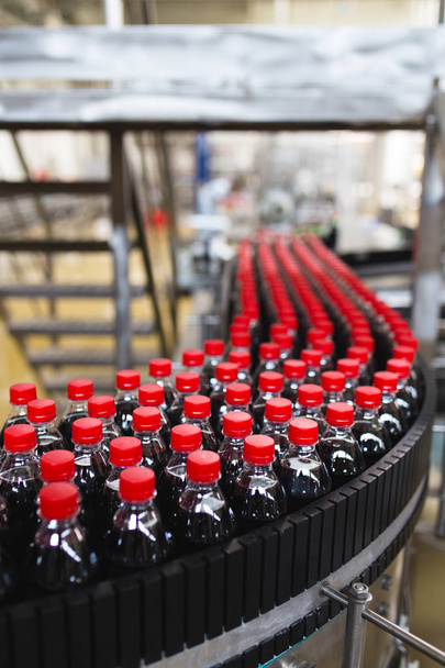 Fábrica de embotellado: línea de embotellado de jugo negro o refrescos para procesar y embotellar jugo en botellas. Enfoque selectivo
.  - Foto, imagen