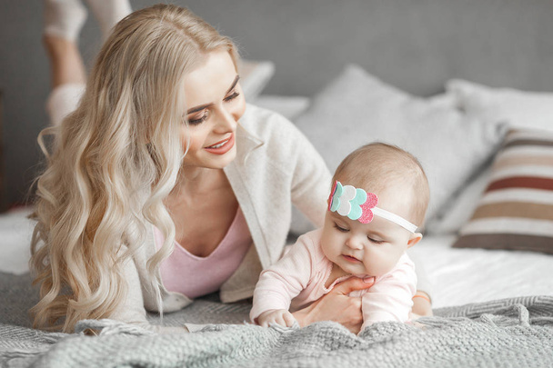 Young mother taking care of her little baby girl. Beautiful mom and her daughter indoors in the bedroom. Loving family. Attractive mum holding her child. - Foto, Bild