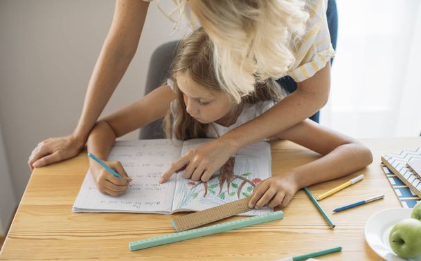 Cute blonde Caucasian girl writing with her mother helping. - Foto, immagini