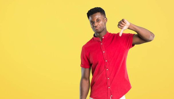 Young african american man showing thumb down sign with negative expression. Sad expression on yellow background - Foto, afbeelding