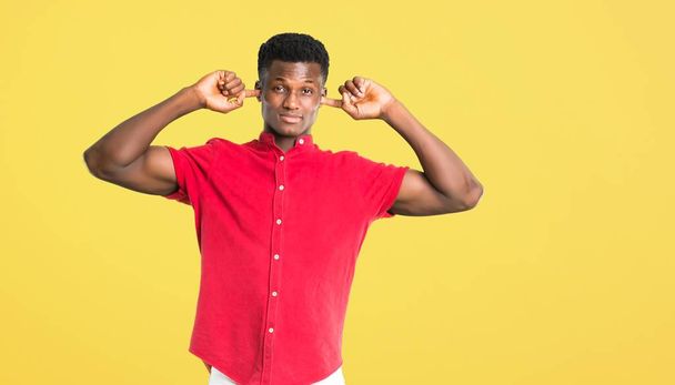 Young african american man covering both ears with hands on yellow background - Foto, imagen