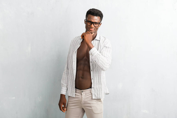 Jonge afro-Amerikaanse man met bril poseren op getextureerde grijs muur - Foto, afbeelding