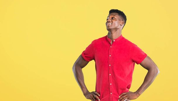 Young african american man posing with arms at hip and laughing on yellow background - Фото, зображення