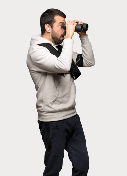 Sport man and looking in the distance with binoculars over isolated grey background - Foto, afbeelding