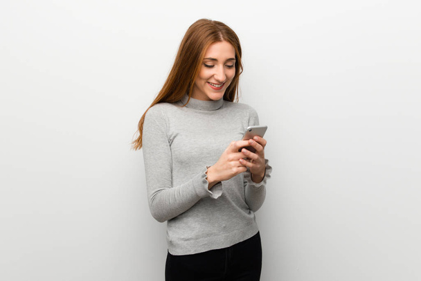 Kızıl saçlı kız beyaz duvar mobil ileti gönderme - Fotoğraf, Görsel