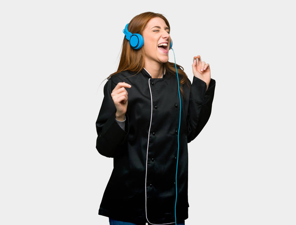 Young redhead chef woman listening to music with headphones on isolated grey background - Foto, imagen