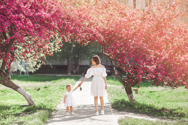 Giovane madre e sua figlia che camminano insieme nel parco nel periodo primaverile. Famiglia felice all'aperto. Amare con adorabile bambina
. - Foto, immagini