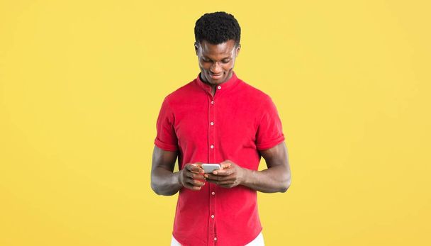 Young african american man sending a message or email with the mobile on yellow background - Zdjęcie, obraz