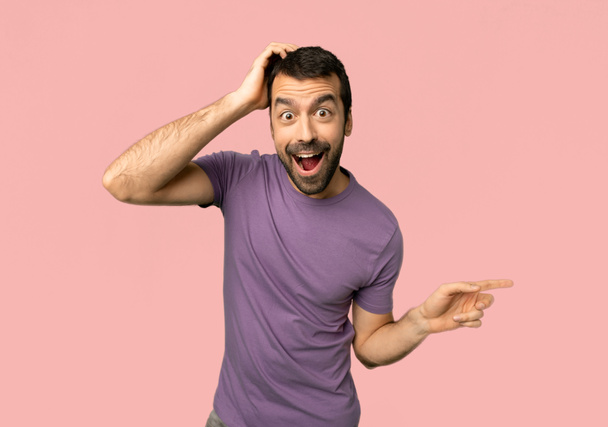 Handsome man pointing finger to the side and presenting a product on isolated pink background - Фото, зображення