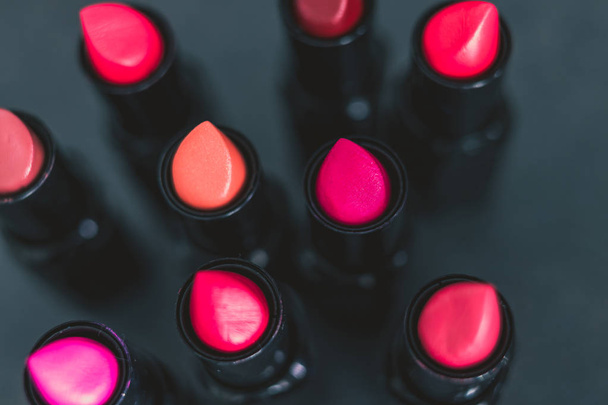 group of red pink and nude lipsticks with different colors and textures on dark table, close-up shot with shallow depth of field - Фото, изображение
