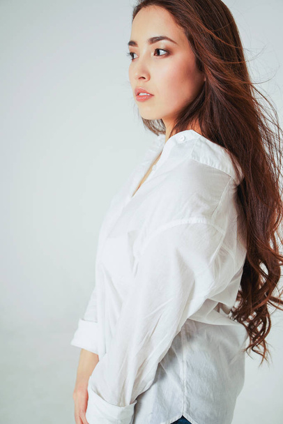 Красота моды портрет улыбающейся чувственной азиатской молодой женщины с темными длинными волосами в белой рубашке на белом фоне
 - Фото, изображение