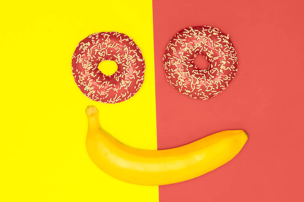 Good mood, smiles food concept. Donuts and a banana in the form of a smiling face. Living coral flat lay. - Photo, Image
