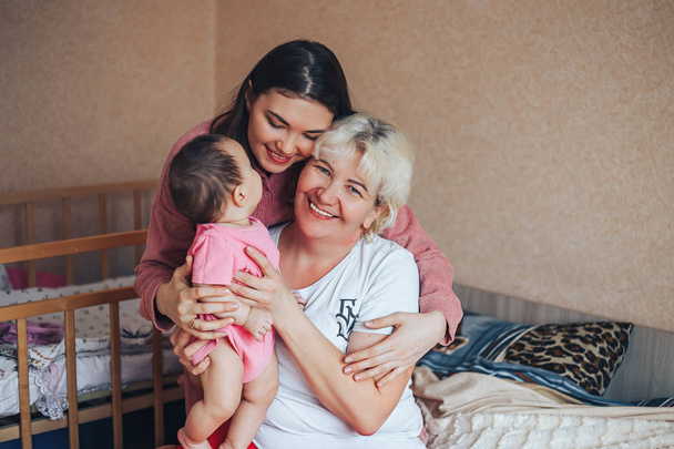 Little cute girl, her attractive young mother and charming grandmother are spending time together at home. Women's generation. Happy International Women's Day - Photo, image