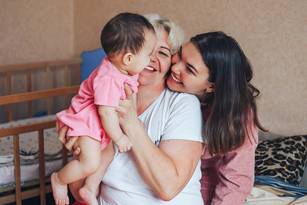 Little cute girl, her attractive young mother and charming grandmother are spending time together at home. Women's generation. Happy International Women's Day - Foto, afbeelding
