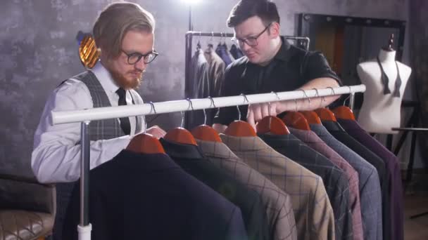 Prodávající pomáhá mladý muž si vybrat oblek v úložišti - Záběry, video