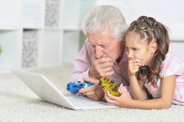 Emotional grandfather and granddaughter playing computer game with laptop - Foto, Imagem