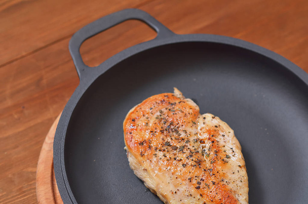 Fried chicken fillet is lying on a frying pan on a wooden table - Photo, Image