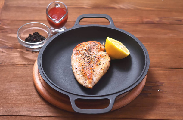 On a frying pan is a fried chicken breast with lemon, spices and a saucepan - Fotografie, Obrázek