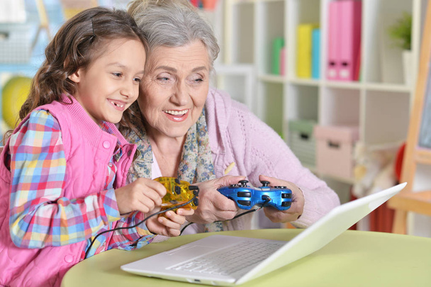 granny with her granddaughter playing computer game on laptop at home - Фото, зображення