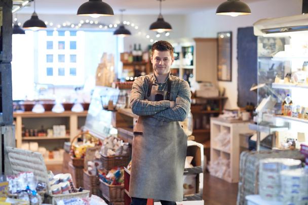 Portret van glimlachen mannelijke eigenaar van Delicatessen winkel schort dragen - Foto, afbeelding