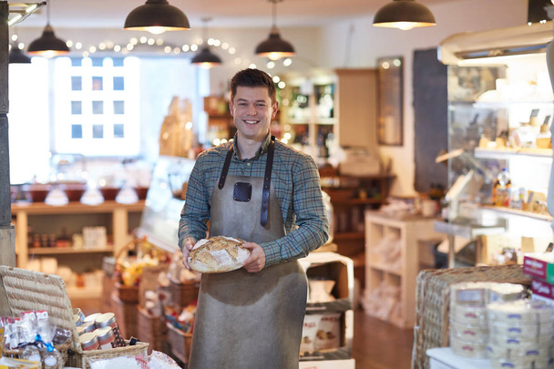 Портрет усміхненого чоловіка власника магазину делікатесів носіння фартуха тримає хліб
 - Фото, зображення