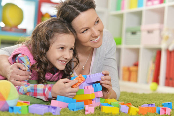 Kręcone mała dziewczynka i jej matka bawi się w domu kolorowe bloki z tworzyw sztucznych - Zdjęcie, obraz