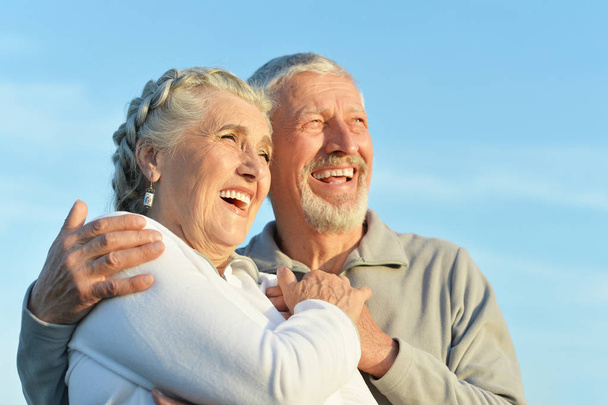 Gelukkige senior paar knuffelen tegen blauwe hemel - Foto, afbeelding