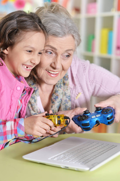 oma met haar kleindochter spelen van computerspel op laptop thuis - Foto, afbeelding