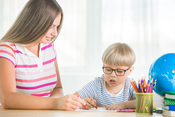Adorable child studying with his mother at home. Family doing homework together. Young mom helping her son to learn a task. - Zdjęcie, obraz