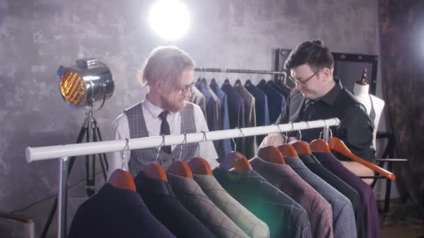 Koncept nákupu. Prodávající pomáhá mladý muž si vybrat oblek v úložišti - Záběry, video