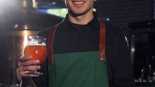 Cervejeiro irreconhecível em avental mostrando polegares para cima, segurando um copo de cerveja
 - Foto, Imagem