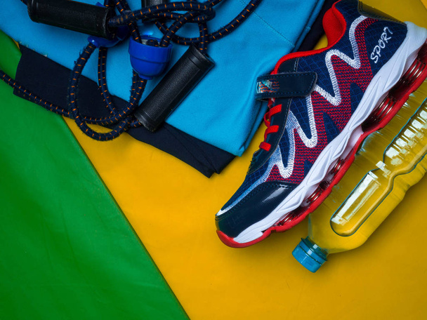 Creative flat lay of sport and fitness equipments clothes, shoe, water, expander on yellow green sport mat background with copy space - Photo, Image