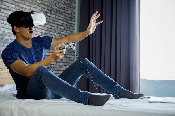Mladý muž v ložnici hraje video hry virtuální realita - Fotografie, Obrázek