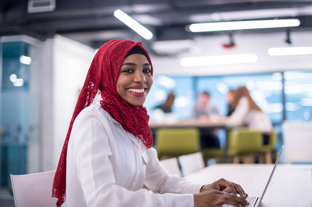 Young modern black muslim business woman wearing a red hijab,working on laptop computer in startup office. Diversity, multiracial concept - Foto, imagen