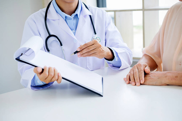 Patient listening intently to a male doctor explaining patient symptoms or asking a question as they discuss paperwork together in a consultation - Photo, Image