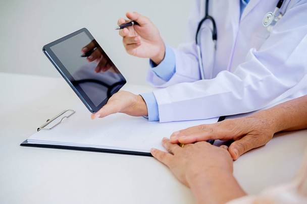 Patient hört aufmerksam zu, wie ein männlicher Arzt die Symptome des Patienten erklärt oder eine Frage stellt, während sie in einer Konsultation gemeinsam den Papierkram besprechen - Foto, Bild