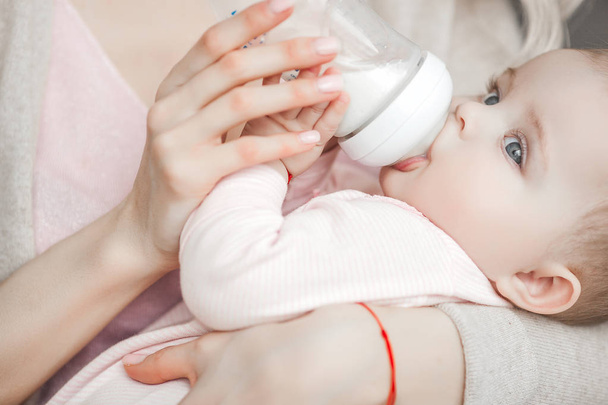Young mother feeding her little cute baby daughter with bottle of child formula. Woman with her newborn baby at home. Mom taking care of a child. Alternative to breast feeding.  - Photo, Image