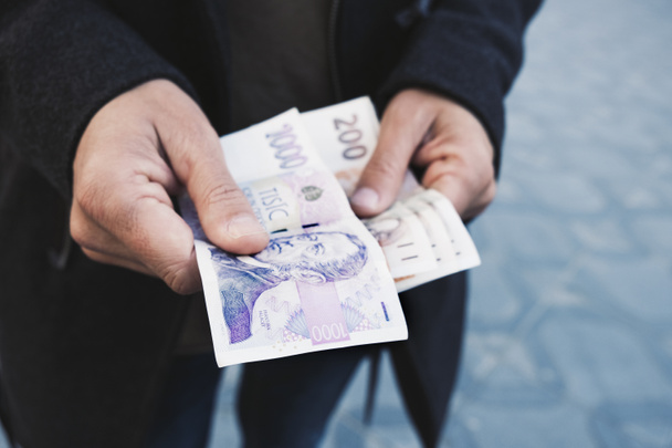 closeup of a young caucasian man on the street offering some czech koruna banknotes to the observer - Photo, Image